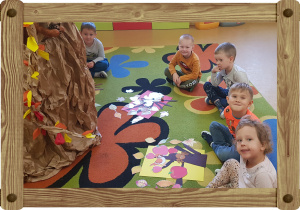 Dzieci siedzą na dywanie, przed nimi kolorowe kartony z ułożoną kompozycją.